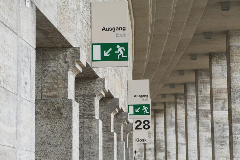 Zwei Hinweisschilder für Fluchtwege an einem Gebäude mit mehreren Durchgängen