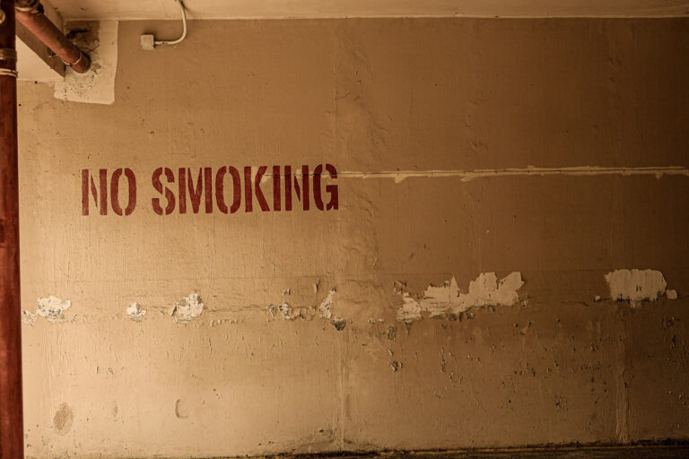 Wand in einem alten Parkhaus mit der Aufschrift "No smoking" , an der Wand platzt an mehreren Stellen bereits die Farbe ab
