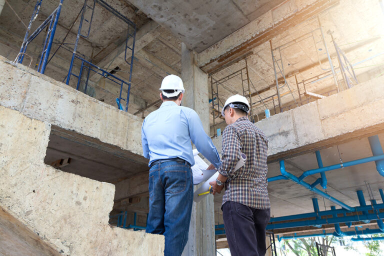 Architekten auf einer Baustelle diskutieren mit Bauplänen in der Hand