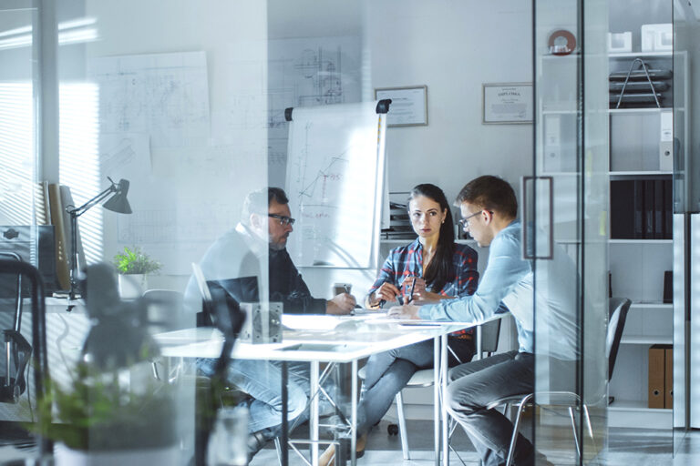 Drei Menschen sitzen in einem Büro und diskutieren über Pläne und Ideen