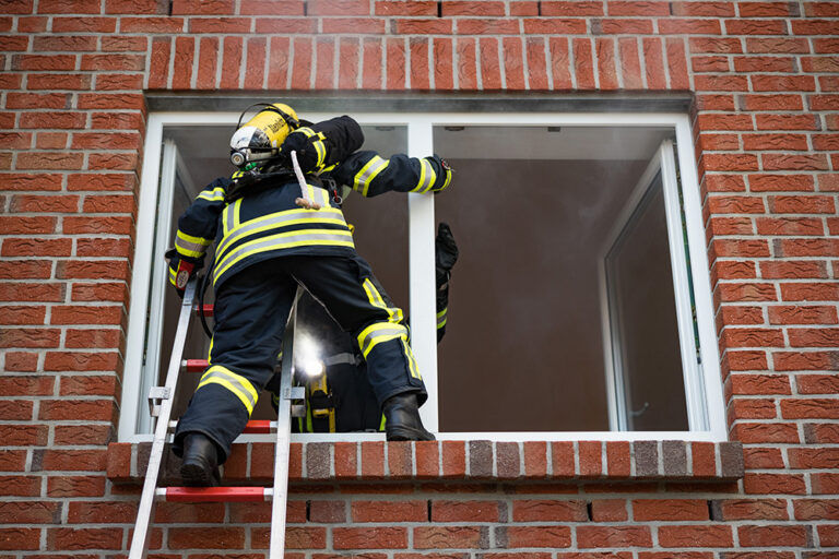 Feuerwehrmann mit Atemschutz klettert über eine Leiter in ein Gebäude
